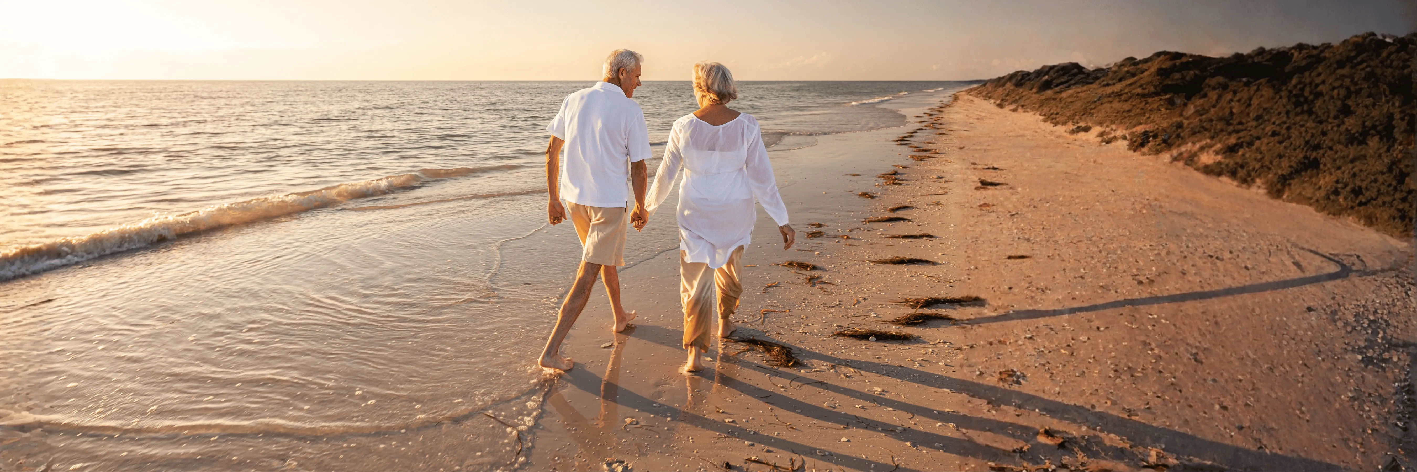 Couple walking on beach at sunset — retirement planning